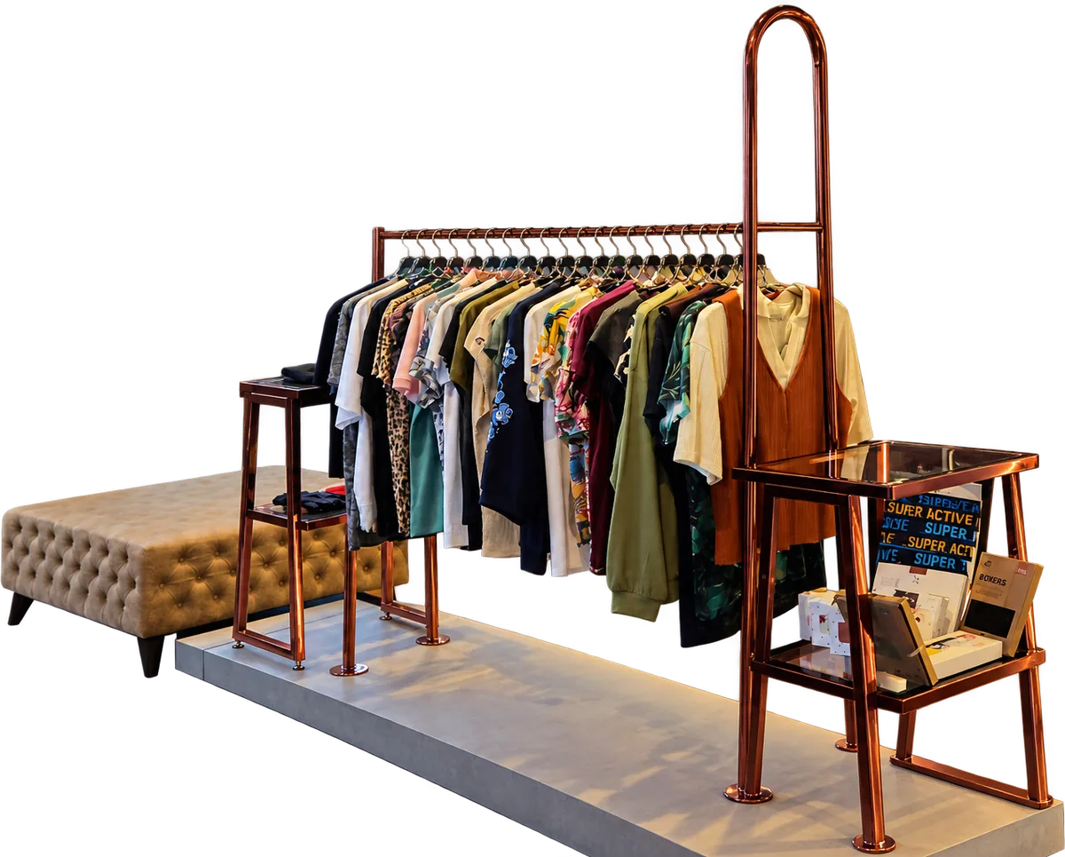 A boutique display of finished knitwear: garments on copper rails above a tufted bench and a cowhide rug