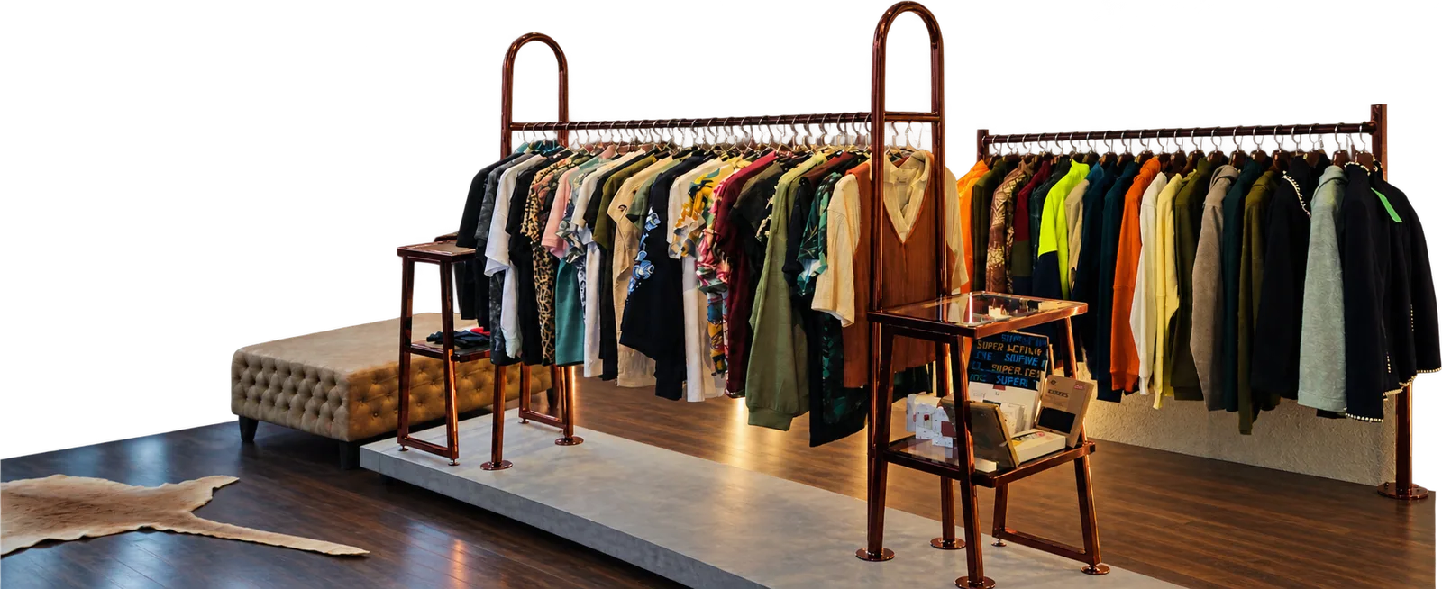 A boutique set on a raised platform: a tufted bench, two copper rails of garments and a shelving stand, over dark wood and a cowhide rug