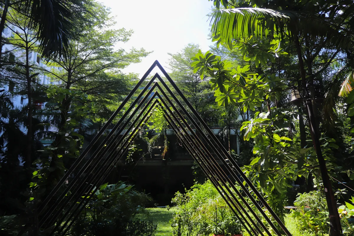 A black triangular sculpture standing among palms in the factory garden