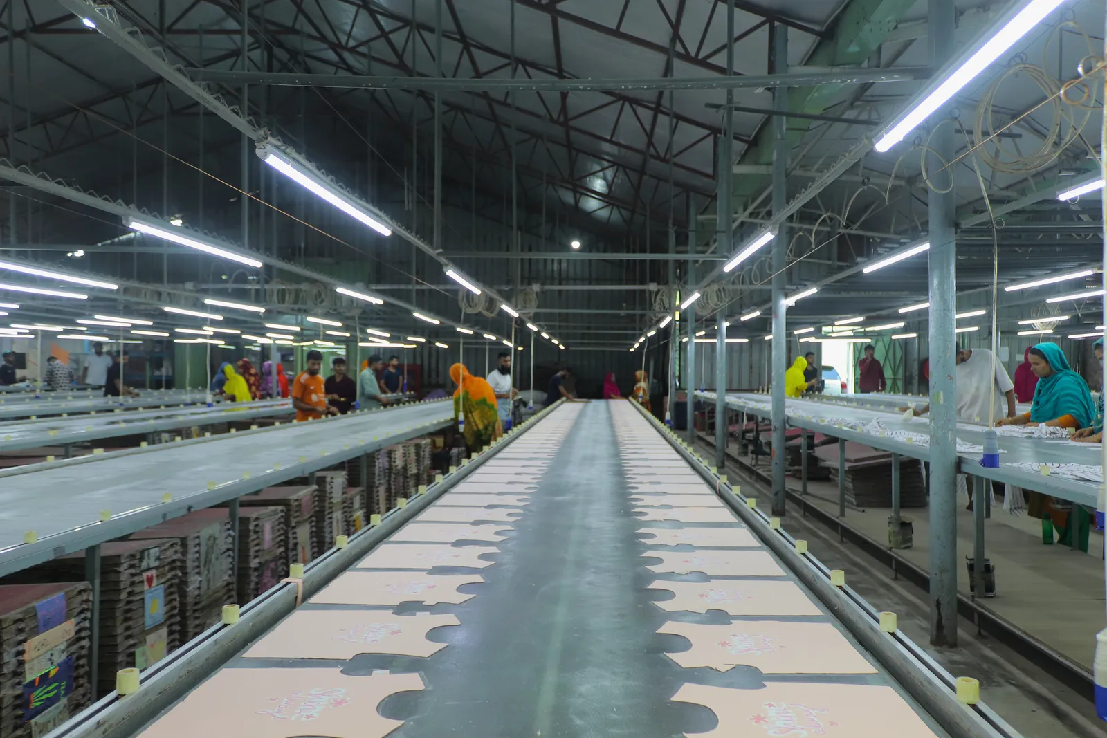 The screen-printing line: long tables of cut garment panels with workers either side under fluorescent tubes