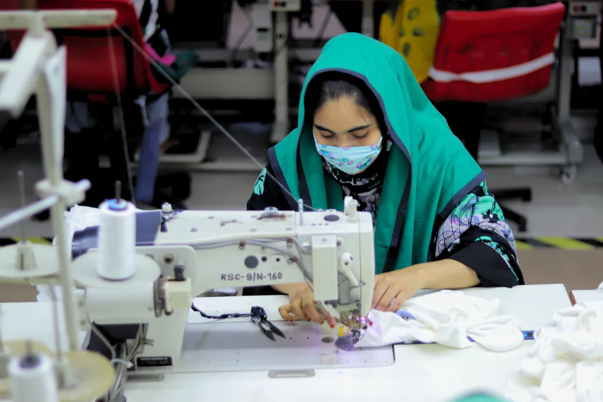 A sewing operator in an emerald-green head covering guiding fabric under the needle