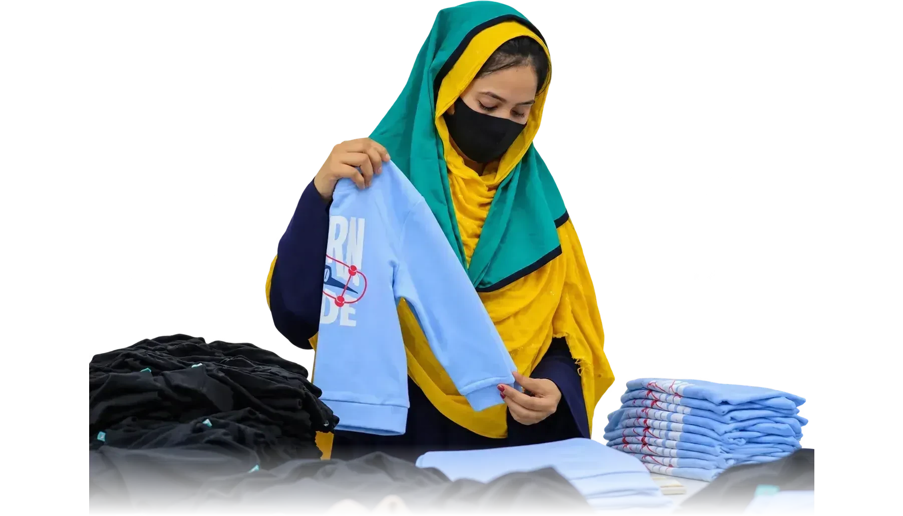 A worker holding up a finished sweatshirt above folded garment piles